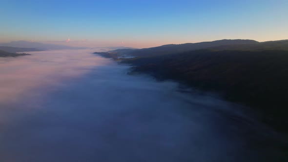 4K aerial view over mountain at sunrise in heavy fog. golden morning sunlight