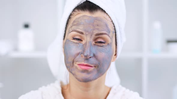 Portrait of Young Woman with Grey Clay Mask on Face Looking at Camera