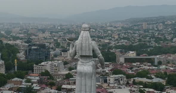 Arc aerial shot of the Kartlis Deda statue with Tbilisi cityscape in the back.