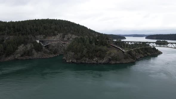 Emerald green waters flow under and around the Deception Pass Bridge, slow aerial orbit