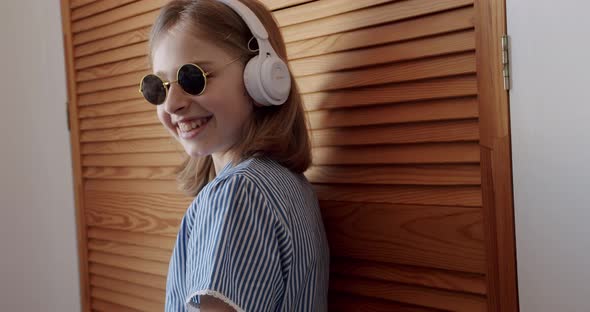 Cute Girl with Round Sunglasses and Wireless Headphones Listening to Music