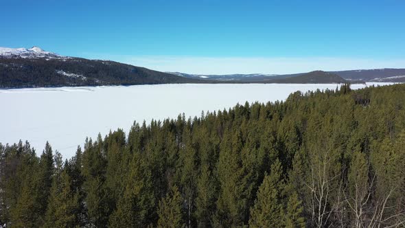 Flying over green spruce forest looking towards ice covered Tunhovdfjorden in Nore and Uvdal Norway