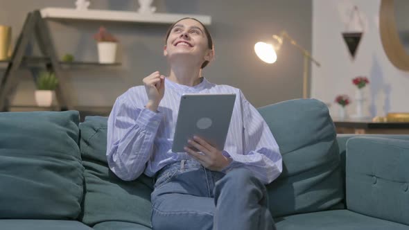 Hispanic Woman Celebrating Success on Tablet on Sofa