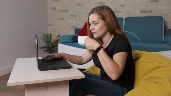 Young Woman Is Drinking a Cup of Coffee While Is Working at the Laptop From Home Office.