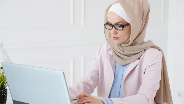 Nerd Muslim Woman in Hijab Is Working on a Graduation Bachelor Project Typing on Laptop and Looking