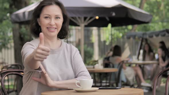 Thumbs Up By Old Woman Sitting in Outdoor Cafe