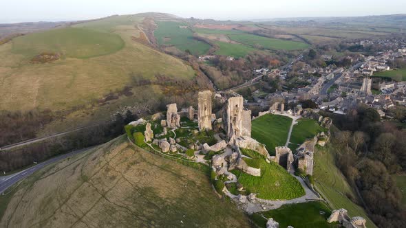 Amazing view of Corfe Castle perched on hill during golden hour. Aerial circling