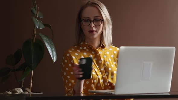 Stylish woman in yellow polka dot shirt using mobile phone and working with laptop computer