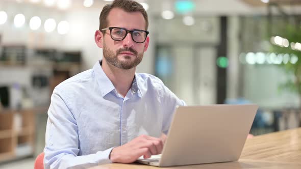 Serious Businessman with Laptop Looking at Camera