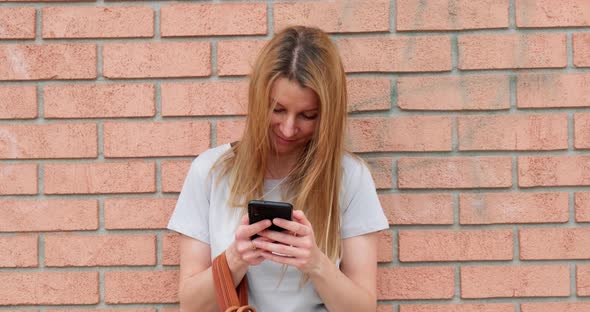 Woman standing by red brick wall and using smartphone.