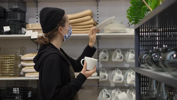 Young Woman Wearing Protective Face Mask Chooses Wooden Pottery in in Dinneware Department of Home