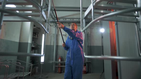 Worker in the paint shop of a metallurgical plant prepares a suspended product for painting