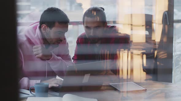 A Young Businessman with a Laptop Talks to a Colleague in the Office