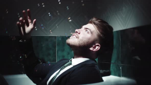 Young Businessman in the Bathtub Plays with Soap Bubbles