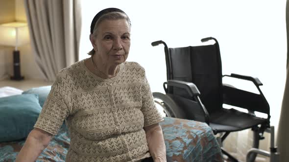 Old Woman Sitting on the Bed Next To the Wheelchair