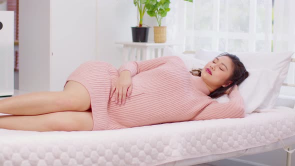Happy Beautiful Pregnant Asian Woman lying on bed smile and sleep