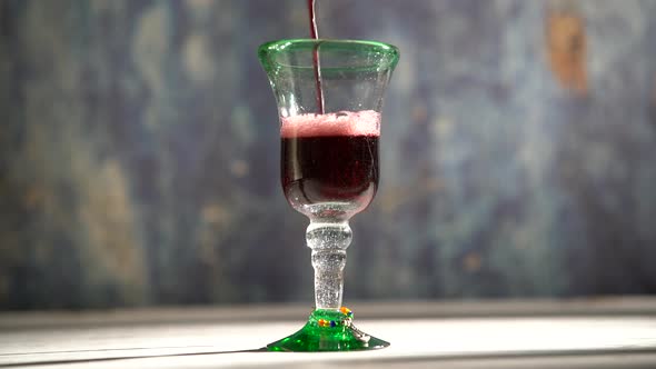 Seamless, looping clip of red wine pouring into a rustic glass with blue background.