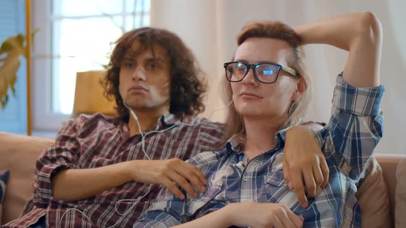 Portrait of Homosexual Male Couple Relaxing on Sofa and Sharing Earphones Listening To Music