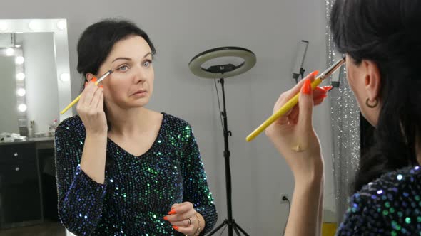 Young Beautiful Showy Woman in Front of the Mirror Applies Face and Eye Makeup with a Special Brush