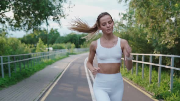 Beautiful Blonde Girl in a White Top and Leggings Jogging in the Park on a Sunny Day