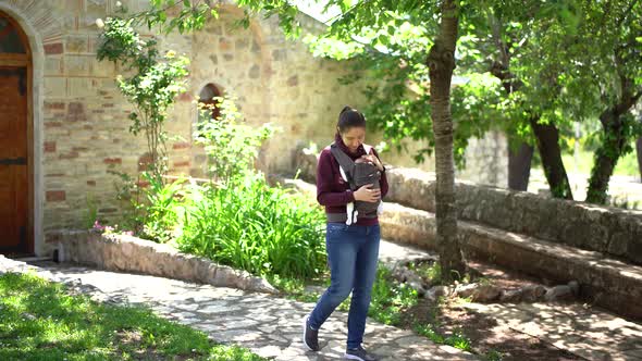 Mom Strokes a Newborn in a Sling While Walking Along the Path in the Park