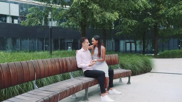 Zoom Shot of Young Man Kissing His Girlfriend's Hand Sitting on Bench in Park