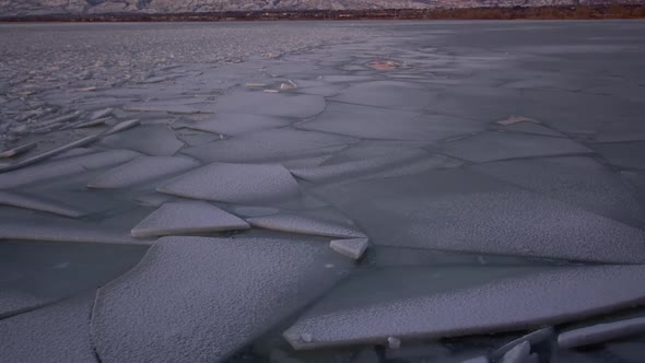Frozen lake surface with cracked iced scattered through the bay at sunset