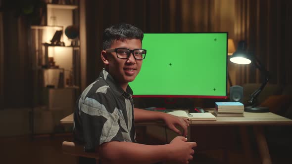Asian Boy Learning Online With Computer Green Screen From Home, He Turns And Smiles Into The Camera
