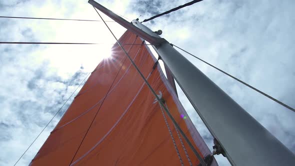 View of Mainsail, Mast and Ropes From Low Angle with Sun Shining Above.