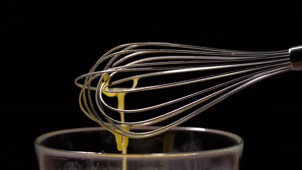 Medium shot of a whisk with dropping beaten eggs in slow motion