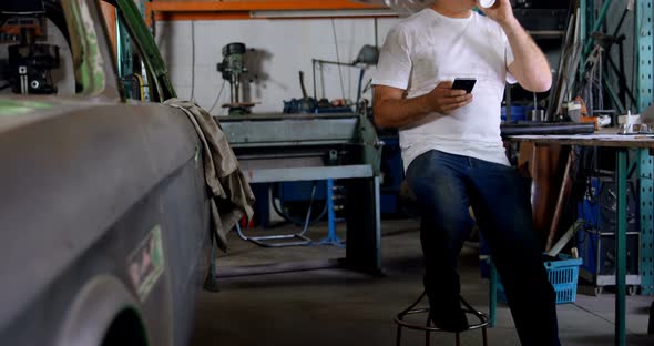 Male mechanic having coffee while using mobile phone 4k