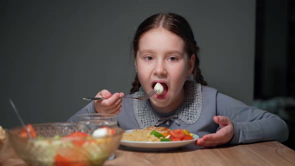 Little girl eats pasta with a fresh salad of tomato, pepper and round cheese