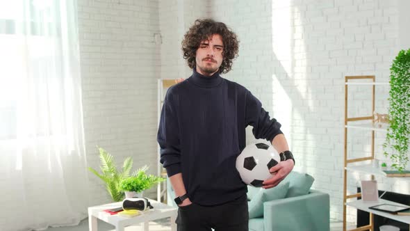 Man Standing with Soccer Ball in Front of the Camera on Bright Room Background