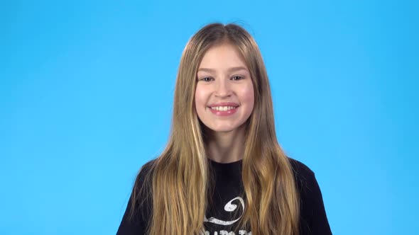 Girl Looking at Camera, Laughing, Posing Against Blue Studio Background.