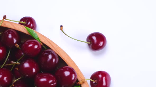 Rotating Wooden Bowl with Ripe Red Cherries on a White Background