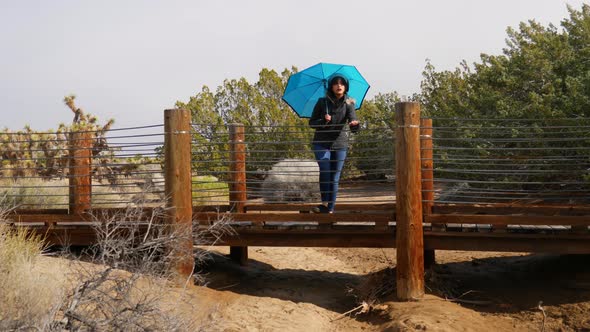 A pretty woman with blue weather umbrella standing on a bridge in a desert nature preserve during a
