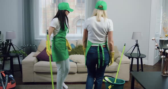 Tired Female Cleaners in Aprons Caps and Gloves Resting on Comfortable Sofa After Finishing Cleaning