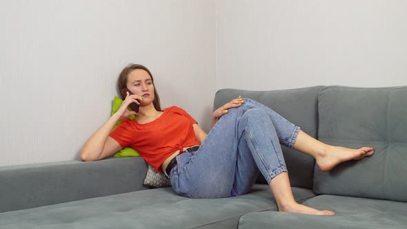 Beautiful young smiling woman talking on the phone while relaxing on the sofa.