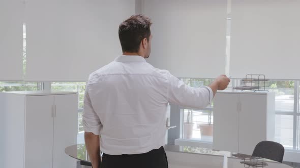 Rear View of Young Businessman Open Window Blinds with Remote Control