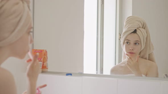 Teenage girl applying lip balm and lip gloss in front of the bathroom mirror