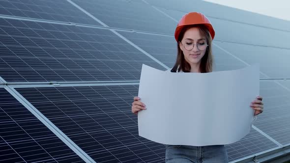 Beautiful young engineer standing near solar panels outdoors, Green Energy Concept.