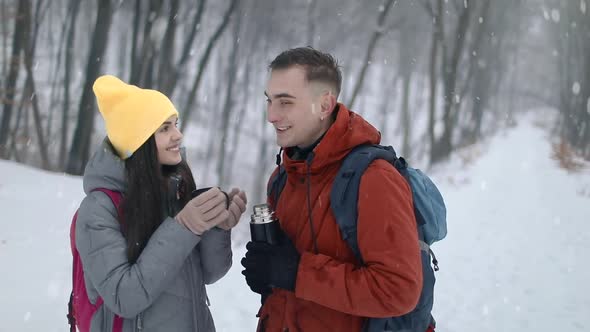 Girl Drinking Tea in Forest with Man Holding Thermos