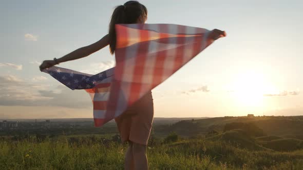 Young woman with USA national flag walking outdoors at sunset. Positive girl celebrating 