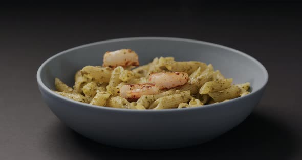 Slow Motion Fried Shrimps Fall on Pest Penne in Blue Bowl on Black Background