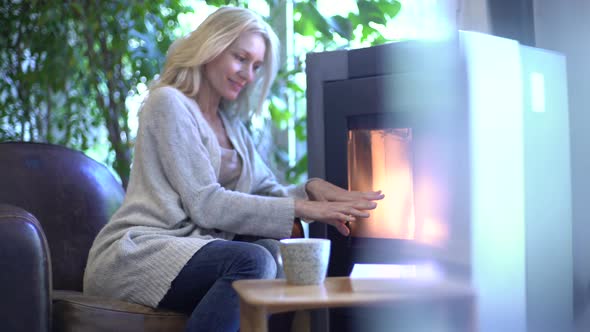 Woman warming hands by fireplace at home