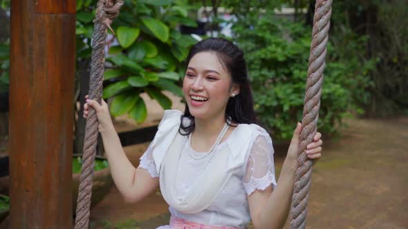 slow-motion of happy young woman in Thai traditional dress relaxing on a wooden swing