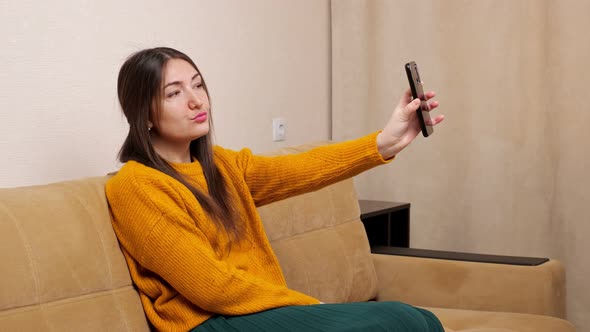 Young Brunette Holds Smartphone and Poses Into Front Camera