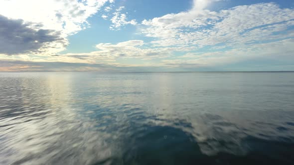 AERIAL: Flying Very Low Above the Surface of Sea into the Horizon with Blue Cloudy Sky