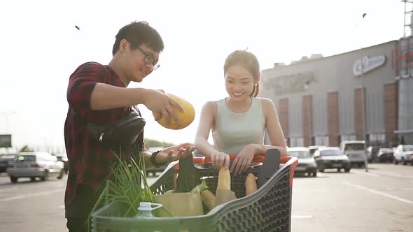 Smiling Vietnamese People Standing Near Market Trolley with Different Products and Enjoying