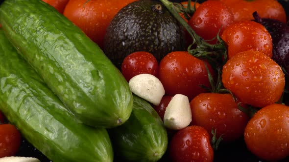 Cherry tomatoes, cucumbers, garlic, avocado and red onion on a black background in water drops